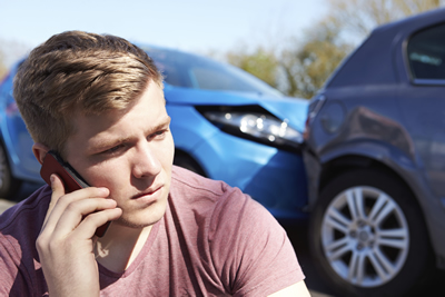 Man on phone with insurance company with two cars that have collided behind him